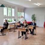 maturzyści siedzący w ławkach. Nauczyciel stojący na pierwszym planie