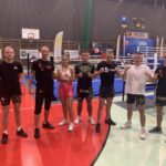 zawodnicy kickboxingu z uczennicą szkoły, która zdobyła mistrzostwo Śląska w tej dyscyplinie stojący na hali sportowej