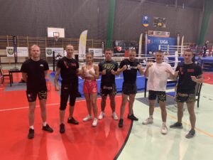 zawodnicy kickboxingu z uczennicą szkoły, która zdobyła mistrzostwo Śląska w tej dyscyplinie stojący na hali sportowej