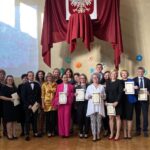 nagrodzoni nauczyciele pozujący do zdjęcia na sali gimnastycznej w tle godło POlski