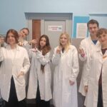 uczniowie pozujący do zdjęcia w fartuchach podczas zajęć w szkolnym laboratorium