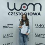 uczennica stojąca z dyplomem na tle makiety "WOM Częstochowa"
