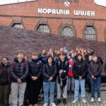 uczniowie stojący przed budenkiem kopalni wujek