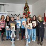 nagrodzeni uczniowie stojący wraz z dyrekcją oraz trzymający nagrody rzeczowe