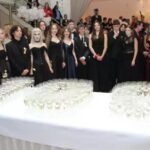 kieliszki z szampanem ułożone w liczbę 100, wokół maturzyści
