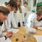 uczniowie w fartuchach uczestniczący w warsztatach z biologii