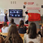 uczniowie podczas lekcji historii, na środku uczeń w przebraniu stojący obok flagii Związku Radzieckiego