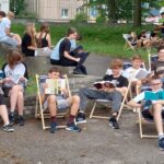 uczniowie siedzący przed gmachem szkoły czytający książkę