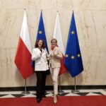 nauczyciele pozujący do zdjęcia na tle flag Polski i UE