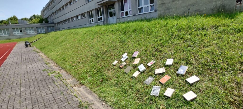 książki położone na trawie przed gmachem szkoły