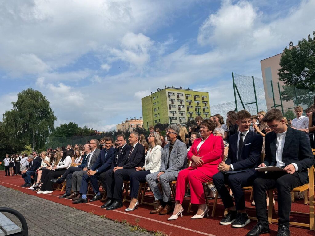 uczniowie i nauczyciele siedzący na boisku szkolnym